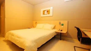 Et hotelværelse med seng, sengebord, stol og en vægmonteret aircondition.