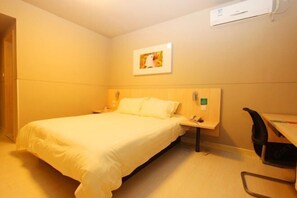 Et hotelværelse med seng, sengebord, stol og en vægmonteret aircondition.