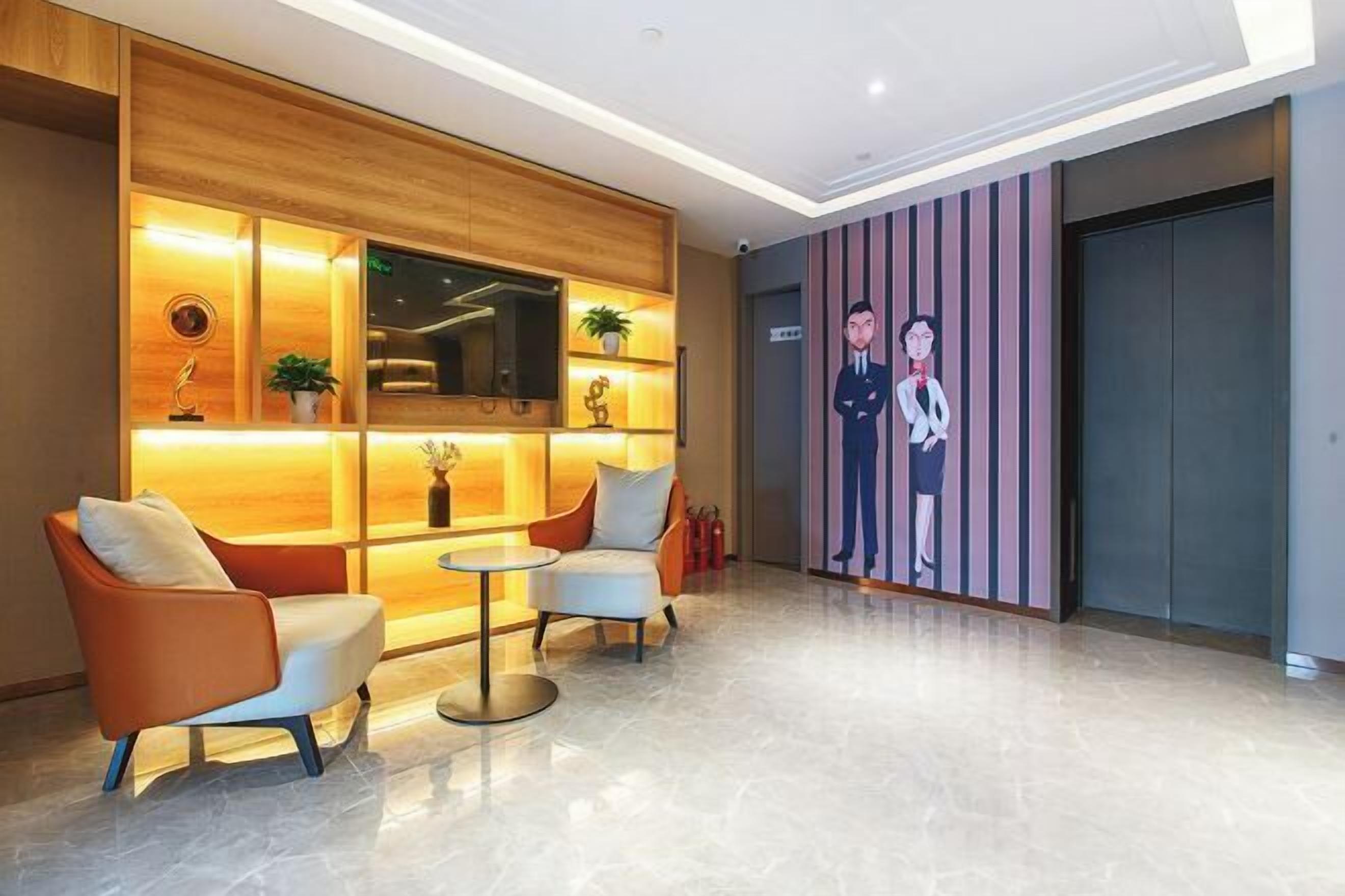 Un vestíbulo con mostrador de recepción de madera, dos sillones, una mesita y un televisor montado en la pared.