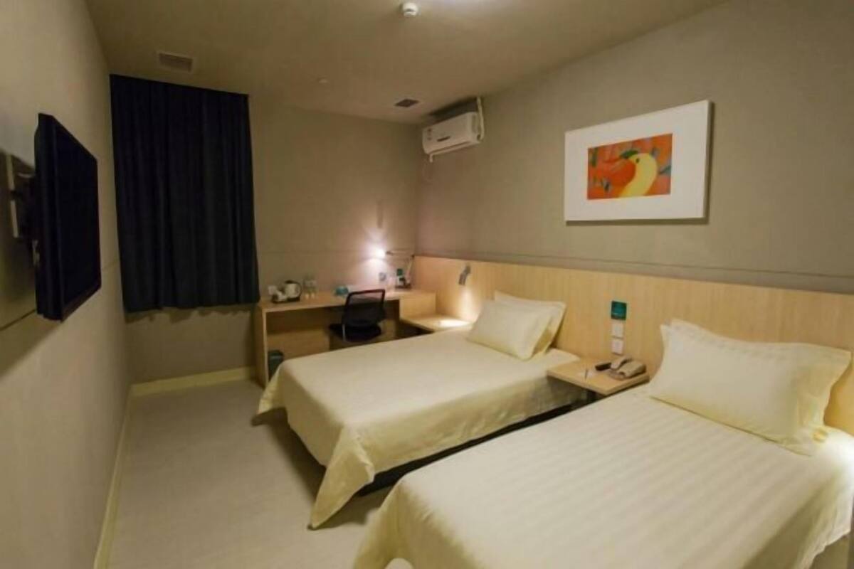 Hotellihuone, jossa on kaksi sänkyä, työpöytä, tuoli, yöpöytä, puhelin ja taulu seinällä.