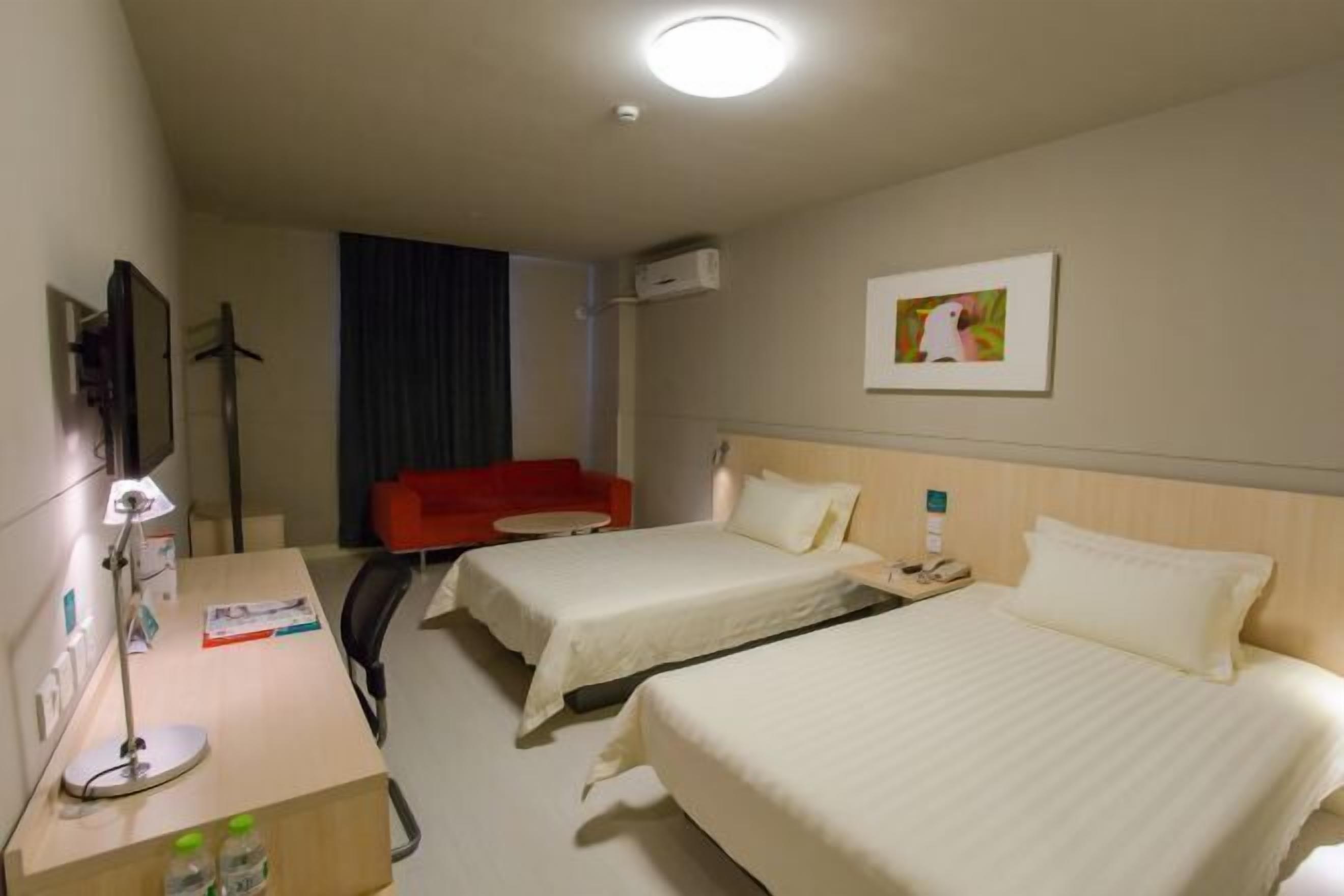 Una habitación de hotel con dos camas, un escritorio con lámpara, una silla roja y un cuadro en la pared.