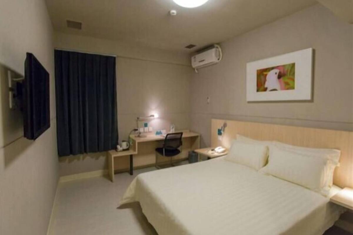 Hotellihuone, jossa on sänky, työpöytä, tuoli ja taulu seinällä.