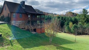 A log cabin with a balcony and a stone foundation, surrounded by a grassy yard and trees. - Misty Mountain Cabin w/ gorgeous views   (Piney Creek)