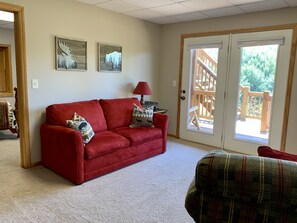 A living room with a red sofa, two decorative pillows, a lamp, and a view of a wooden deck through a glass door. - Misty Mountain Cabin w/ gorgeous views   (Piney Creek)