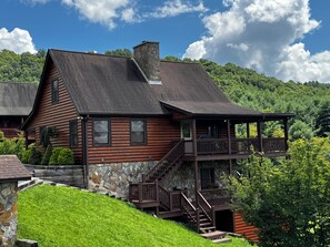 Eine Blockhütte mit einem Steinkamin, einer Veranda und einer Treppe, die zu einer Terrasse führt.