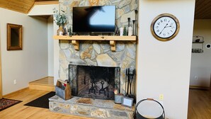 A stone fireplace with a TV above it, a clock on the wall, and a dog bowl on the floor. - Misty Mountain Cabin w/ gorgeous views   (Piney Creek)