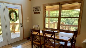 A wooden dining table with four chairs, a window with blinds, a welcome sign, and a wooden deck outside. - Misty Mountain Cabin w/ gorgeous views   (Piney Creek)