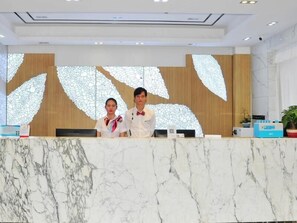 A reception desk with a marble top, two staff members in uniforms, and a large decorative wall with leaf patterns. - Greentree Inn Haikou City Wuzhishan Road (Haikou)