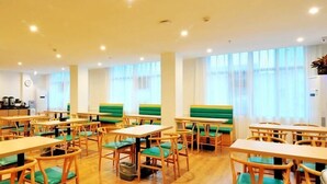 A dining area with wooden tables and chairs, green cushioned benches, and large windows with sheer curtains. - Greentree Inn Haikou City Wuzhishan Road (Haikou)