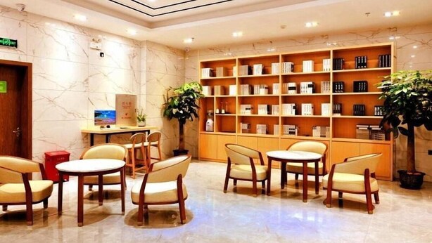 A lobby with marble flooring, wooden chairs, tables, and a bookshelf with books. - Greentree Inn Haikou City Wuzhishan Road (Haikou)