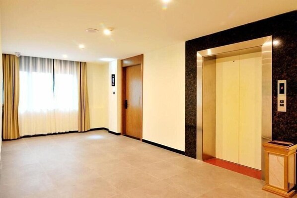 Un couloir d’hôtel avec une porte en bois, un ascenseur et un mur en marbre.