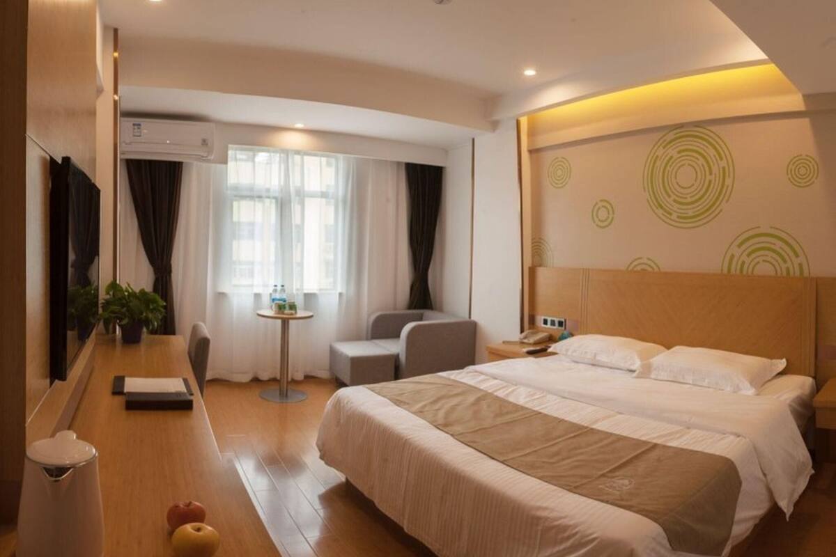 A hotel room with a bed, a desk, a chair, a small table, and a TV.