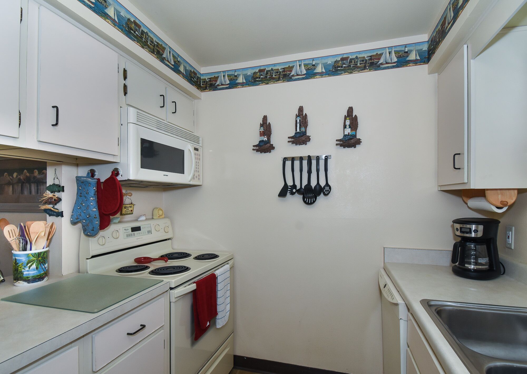 A compact kitchen with white cabinets, a microwave, a stove, and a coffee maker.