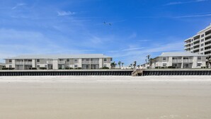 A beachfront hotel with multiple balconies and a sandy beach in the foreground.
