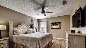 A bedroom with a large bed, a ceiling fan, a nightstand with a lamp, a dresser, and a painting on the wall. - Dreams come true (Kissimmee)