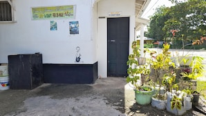 A building with a sign welcoming drifters, a black door, and a concrete ground with potted plants. - Drifters at One Mile - Hostel (Negril)