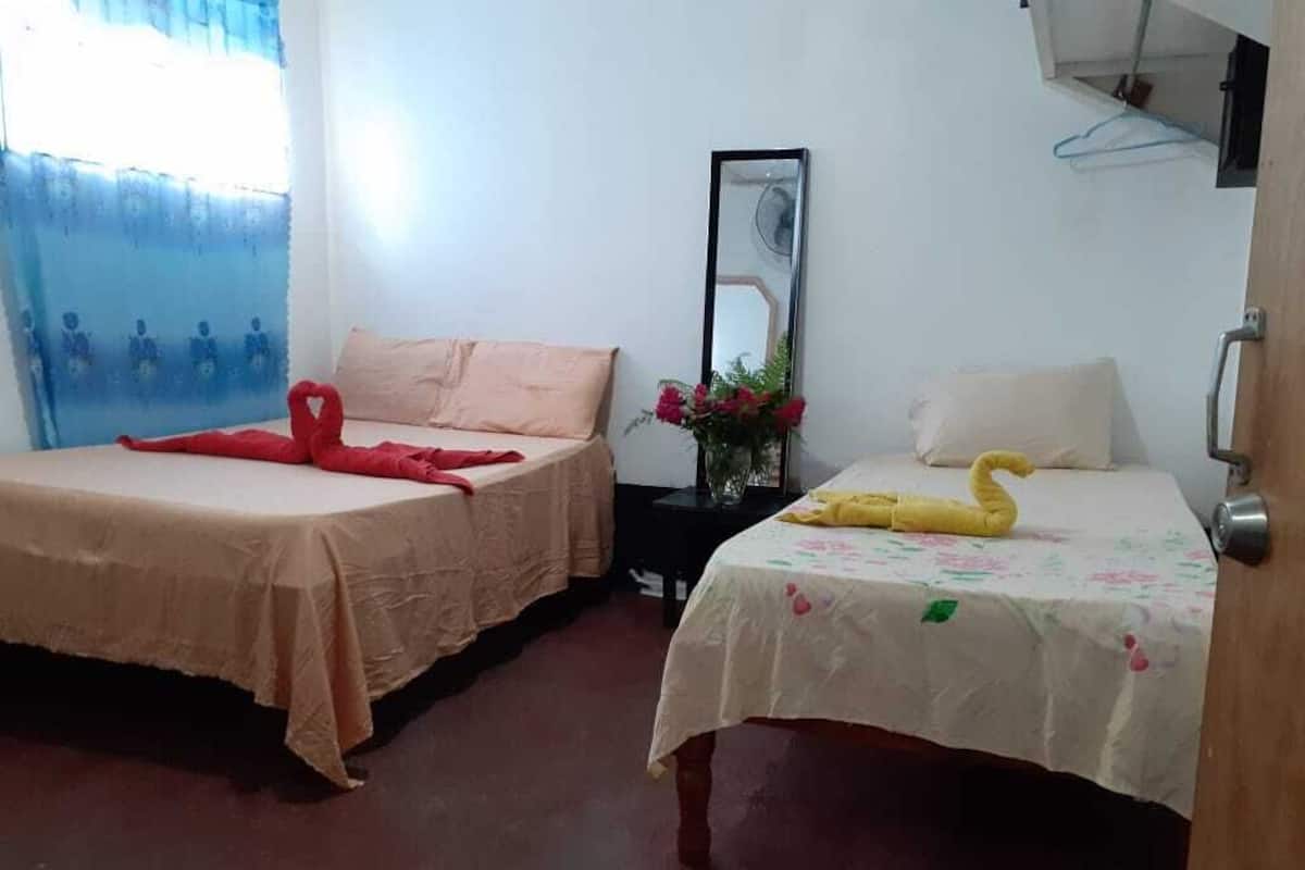 Two beds with different bedspreads, a mirror, and a small table with a vase of flowers.