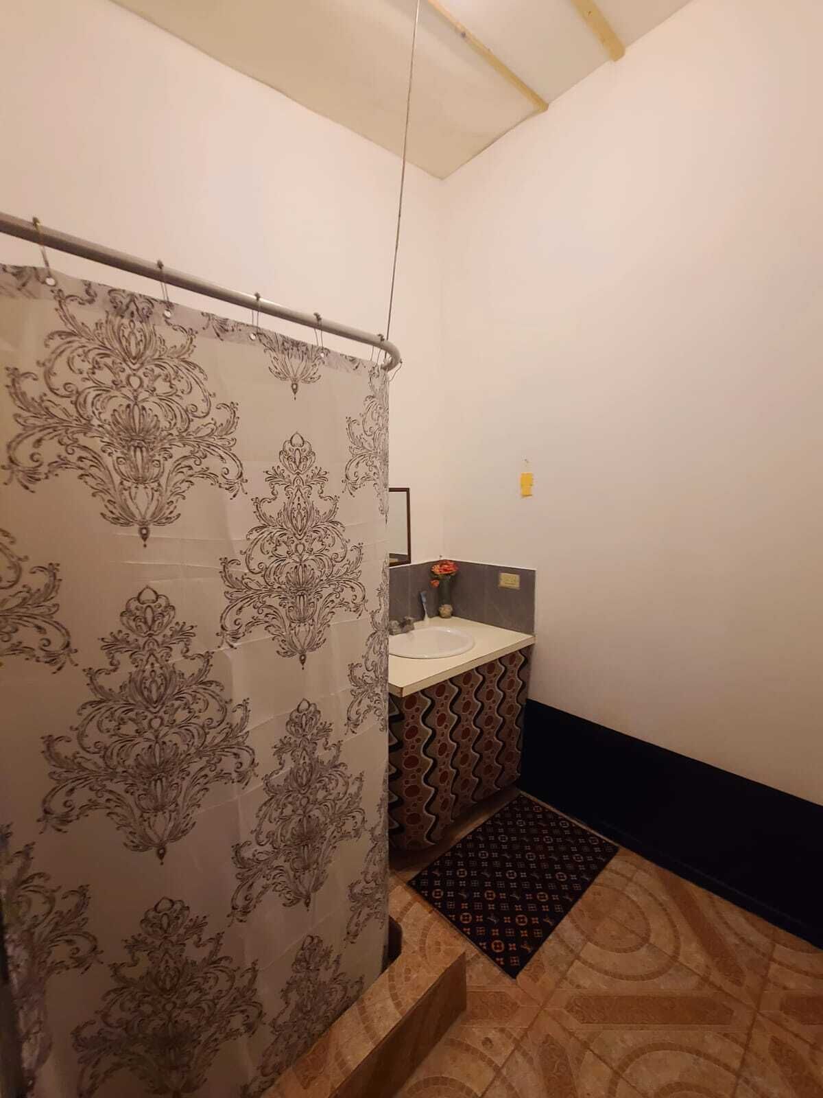Un baño con cortina de ducha estampada, un lavamanos y piso con diseño.