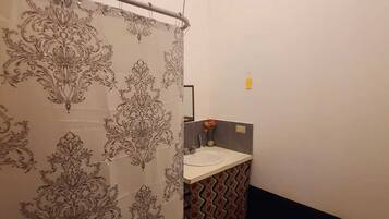 Un baño con cortina de ducha estampada, un lavamanos y piso con diseño.