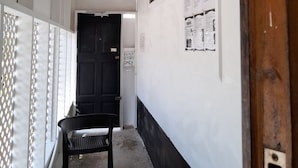 A hallway with a black door, a white wall with posters, a black bench, and a wooden door frame. - Drifters at One Mile - Hostel (Negril)