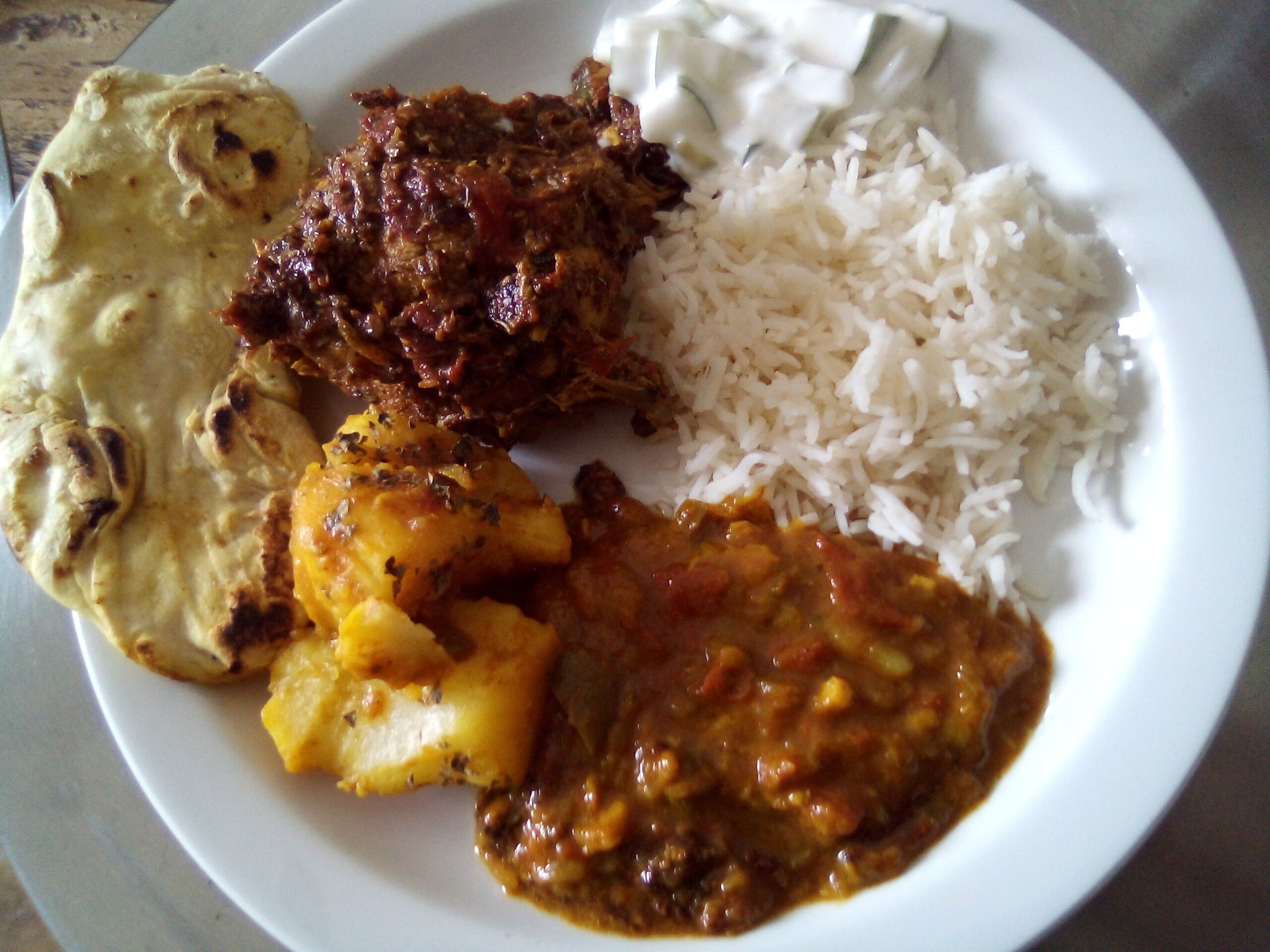 A plate with white rice, a piece of naan bread, and two types of curry.