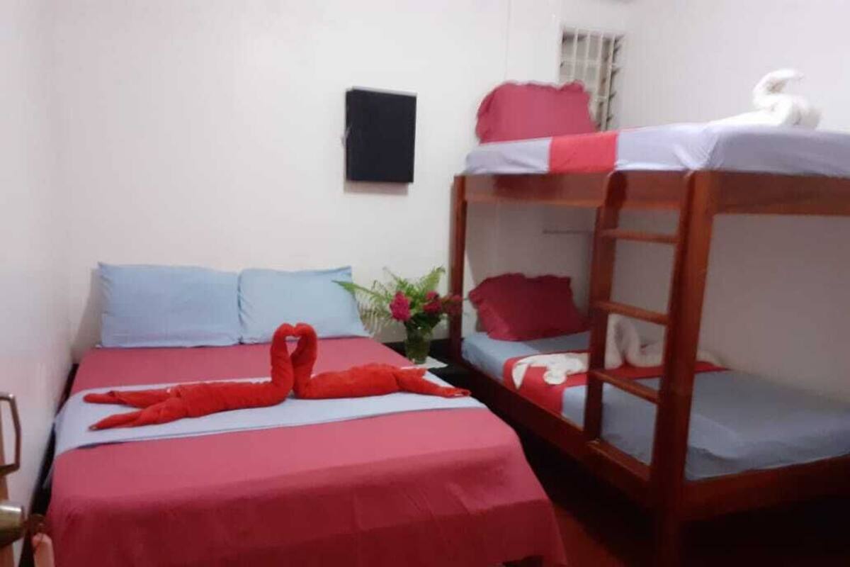 A room with two beds, one with a red blanket and the other with a white and red blanket. There is a small table with a vase of flowers and a white swan decoration on the bed.