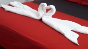 A hotel room with a red bedspread, a white towel arranged in a heart shape, and a red pillow. - Drifters at One Mile - Hostel (Negril)