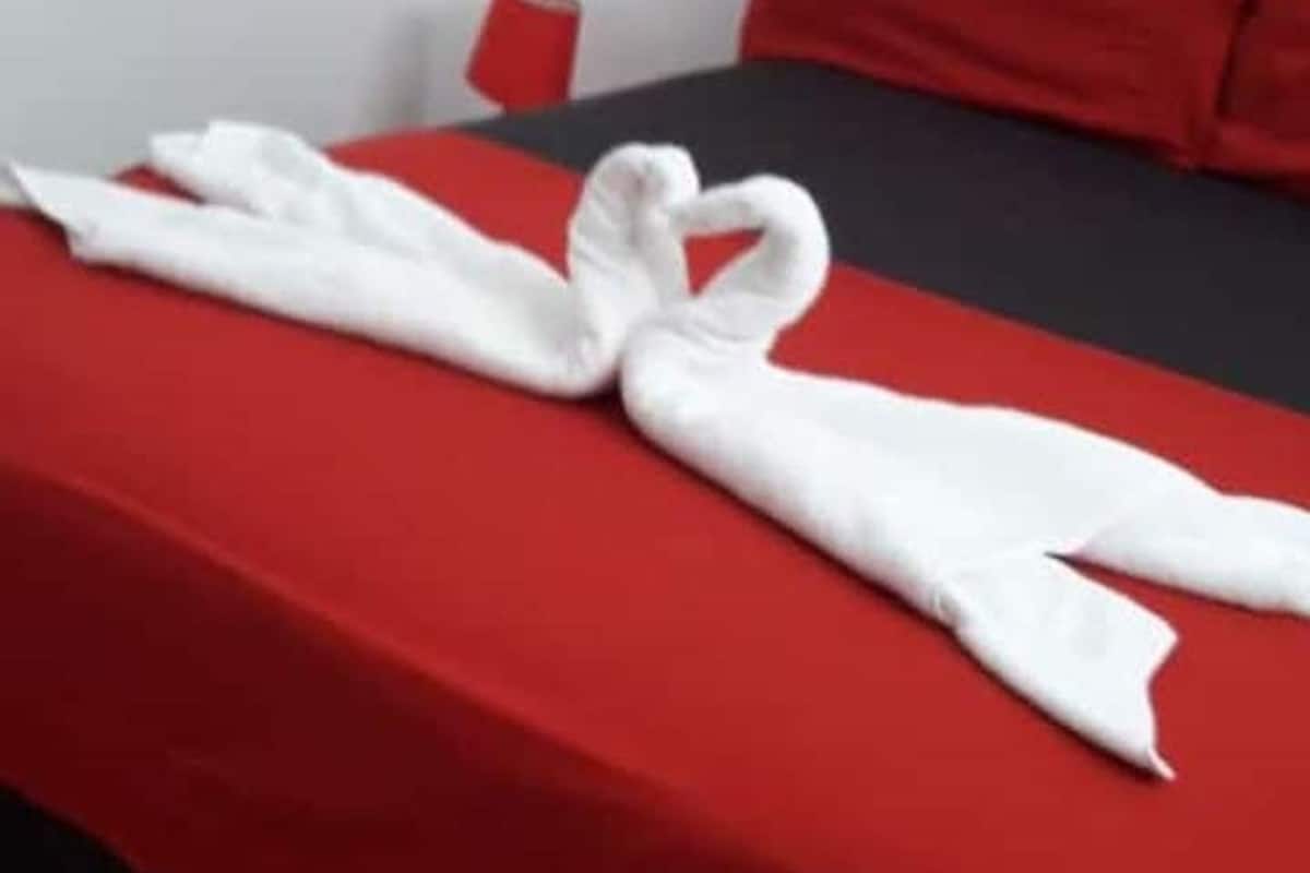 A hotel room with a red bedspread, a white towel arranged in a heart shape, and a red pillow.