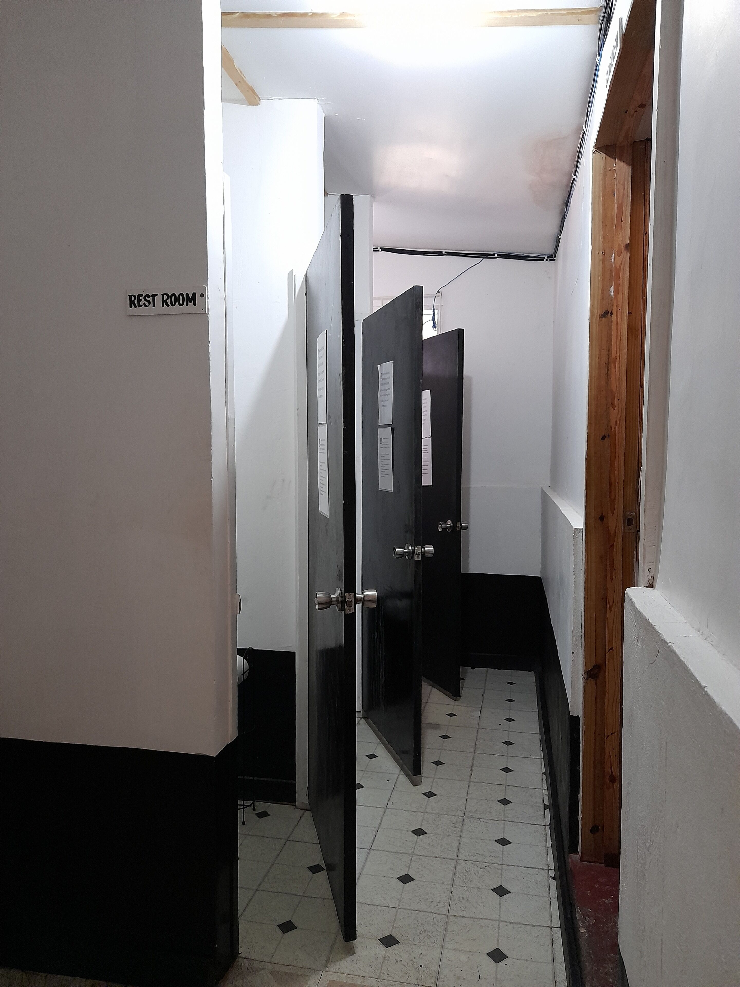 A narrow hallway with a sign indicating a rest room. The walls are white, and the floor has a black and white tile pattern.