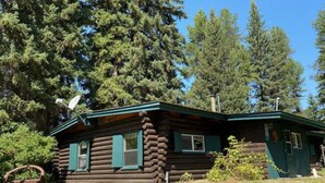 A log cabin with a green roof, surrounded by dense forest. - 1920 Montana Quiet Log Cabin! Creek, fire pit, 10 ac. of wilderness/ Swan Valley (Bigfork)