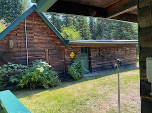 Cozy cabin with a small porch and a birdhouse, nestled among a lush lawn and dense forest.