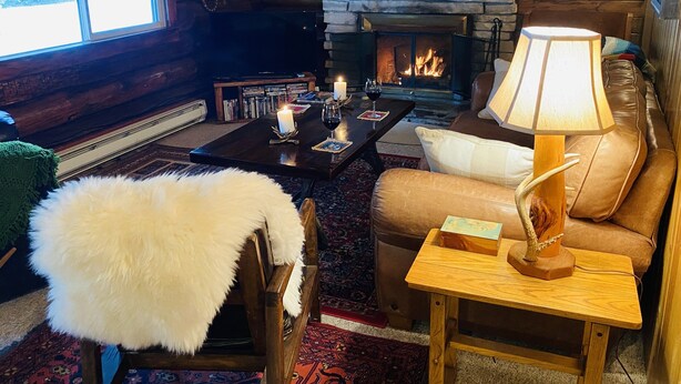 A cozy living room with a fireplace, leather sofa, and a fur throw. - 1920 Montana Quiet Log Cabin! Creek, fire pit, 10 ac. of wilderness/ Swan Valley (Bigfork)