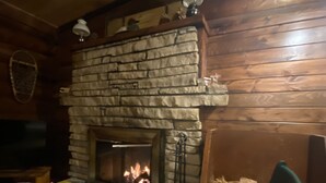 A cozy living room with a stone fireplace, wooden walls, and a television on the left. - 1920 Montana Quiet Log Cabin! Creek, fire pit, 10 ac. of wilderness/ Swan Valley (Bigfork)