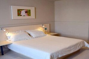A single-bed room with a white headboard, a bedside table, and a wall-mounted lamp.