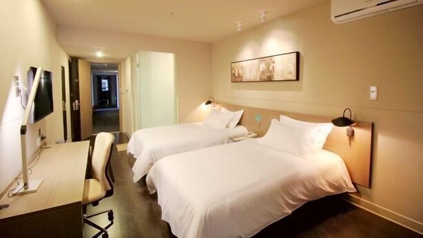 Habitación de hotel con dos camas, un escritorio, una silla, aire acondicionado y un cuadro en la pared.