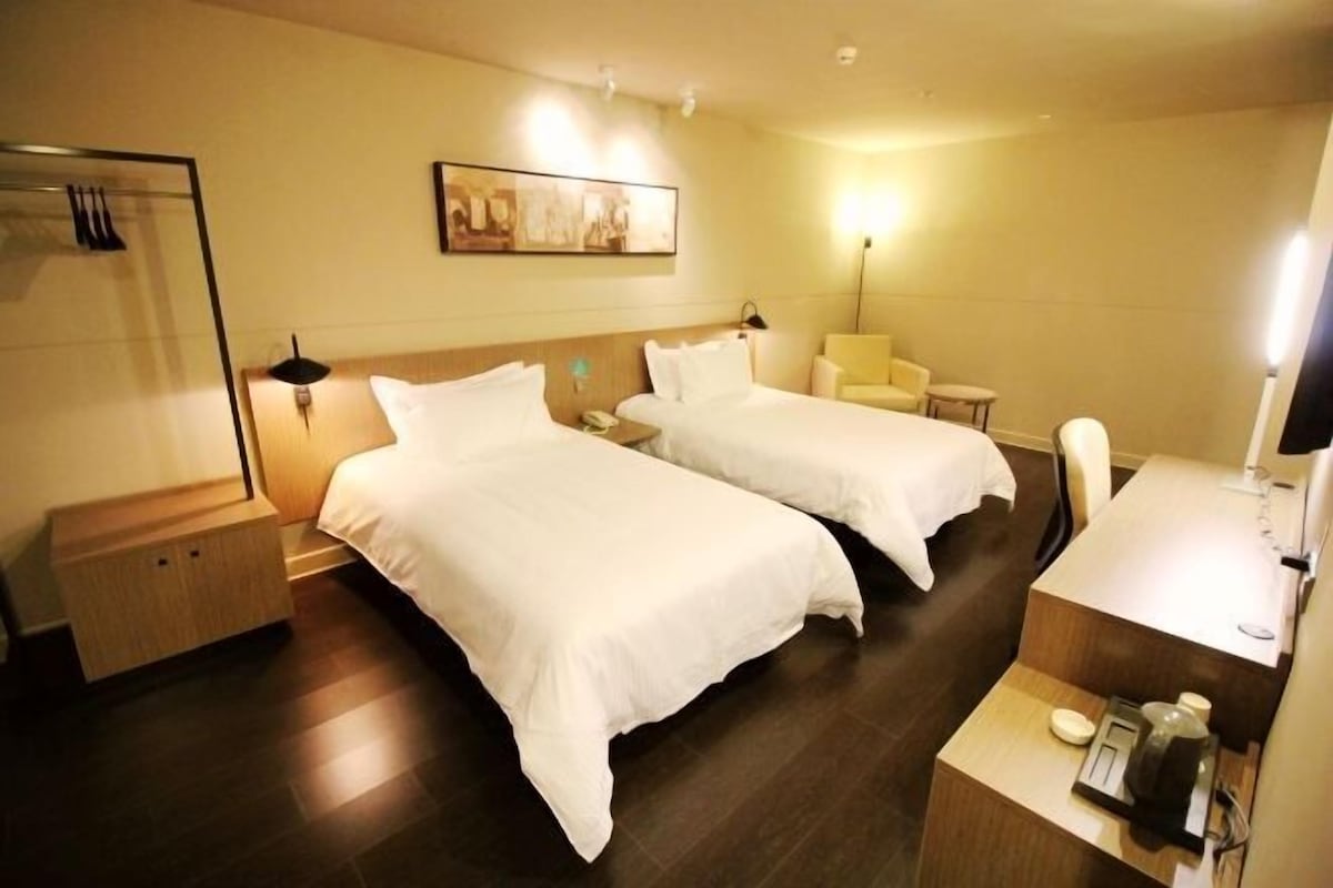 A hotel room with two beds, a bedside table, a chair, a desk, and a wall-mounted artwork.