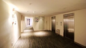 Un pasillo de hotel con piso alfombrado, dos ascensores y una puerta al final.