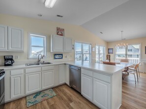A modern kitchen with white cabinetry, a built-in dishwasher, and a large island with seating. - The Channel Marker | Ocean to Sound Views! (Topsail Beach)