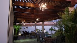 An outdoor patio area with a wooden pergola, seating, and a pool in the background. - Million Dollar View! (Cabo San Lucas)