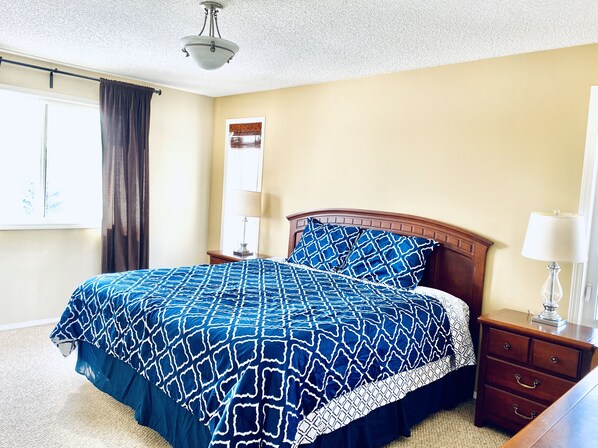 A bedroom with a bed, a nightstand, a lamp, a window with curtains, and a ceiling light. - Spacious 3BR Retreat w/ Hot Tub Ravine | Sleeps 9 (Edmonton)