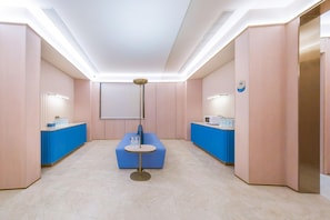 Un hall d’hôtel moderne avec un comptoir d’accueil, un espace détente bleu et un grand écran.