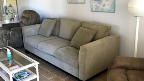 En stue med en grå sofa, et hvidt sofabord med magasiner, og to rammede blomsterbilleder på væggen.