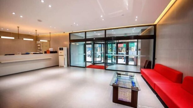 A modern reception area with a glass door entrance, a reception desk, a red sofa, and a coffee table. - Jinjiang Inn (Changchun Railway Station) (Changchun)