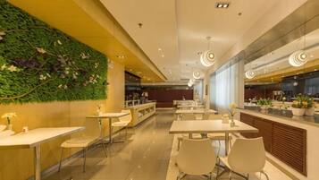 A modern restaurant with a green wall, white tables, and a kitchen area in the background.