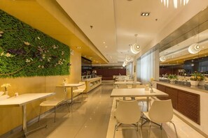 A modern restaurant with a green wall, white tables, and a kitchen area in the background.