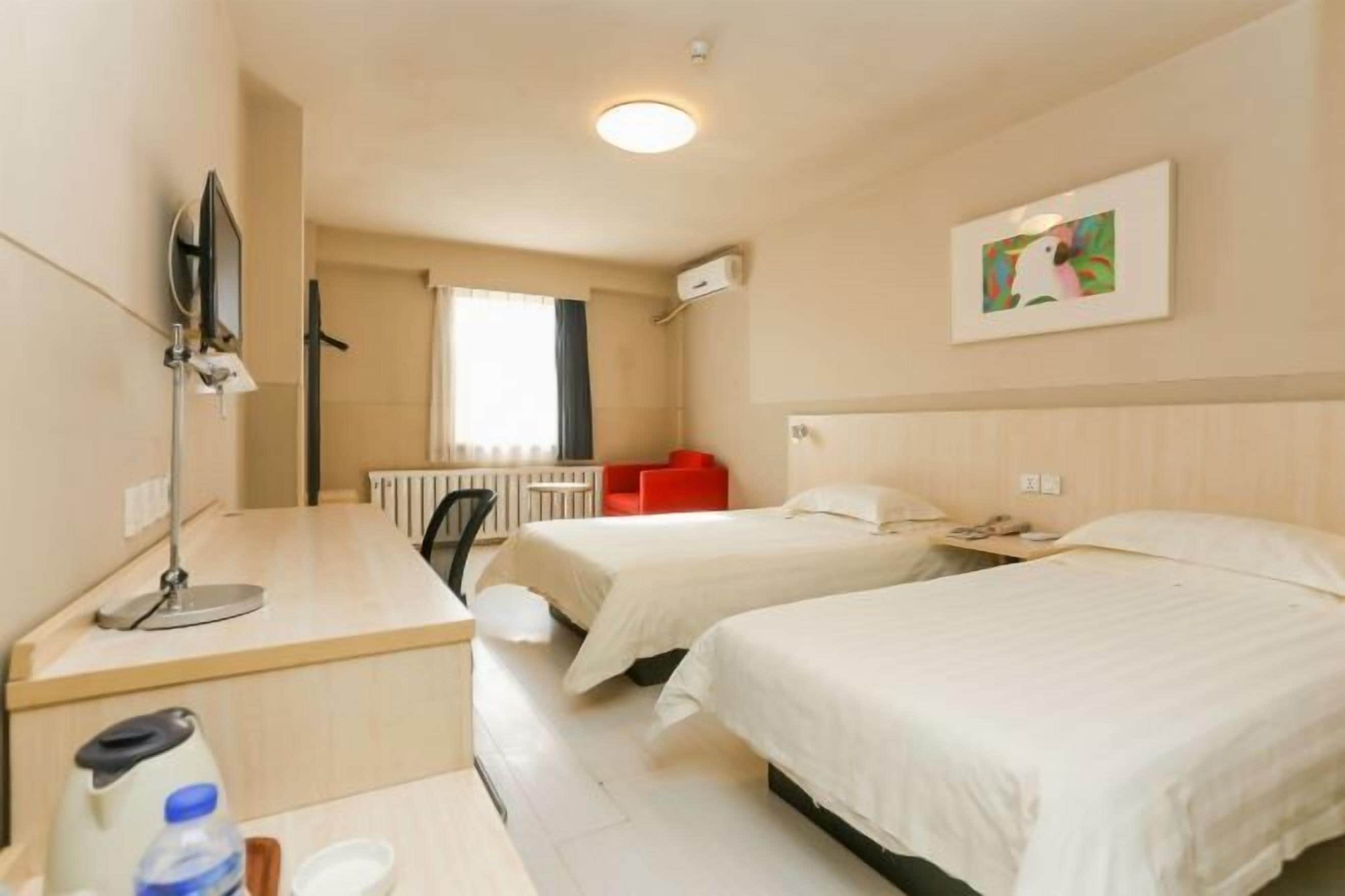 A hotel room with two beds, a desk with a chair, a TV, and a window with curtains.