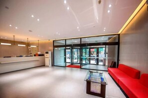A modern hotel lobby with a reception desk, seating area, and glass doors leading to the outside.