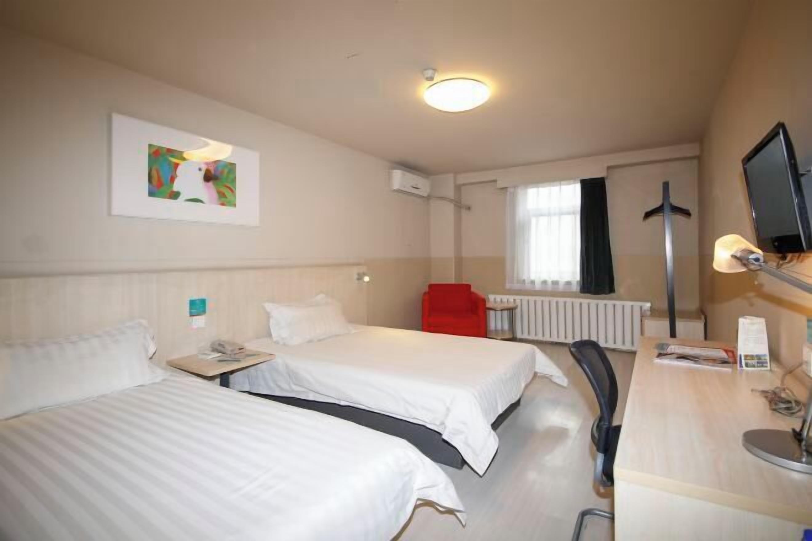 A hotel room with two beds, a desk, a chair, a TV, and a painting on the wall.