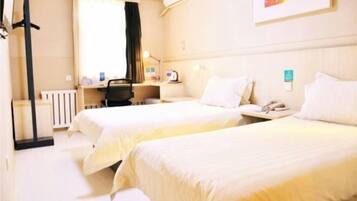 A hotel room with two beds, a desk, a chair, a radiator, and a window with curtains.