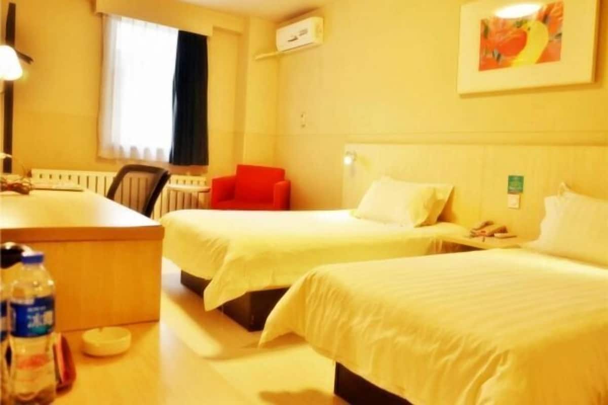 A hotel room with two beds, a desk, a chair, a radiator, and a painting on the wall.